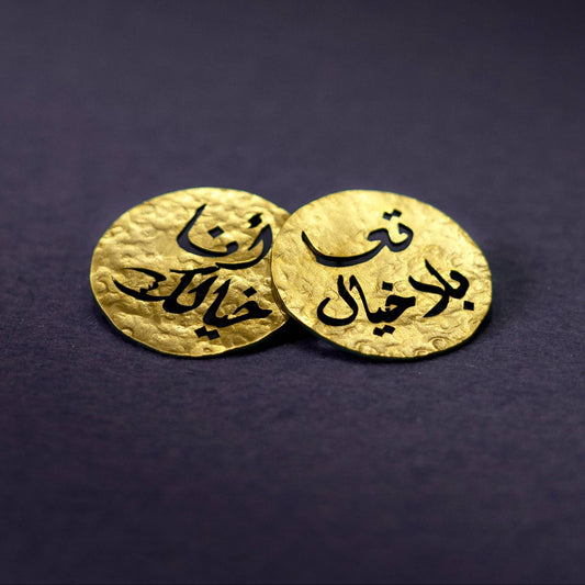 Two gold earrings with Arabic text on a dark purple background
