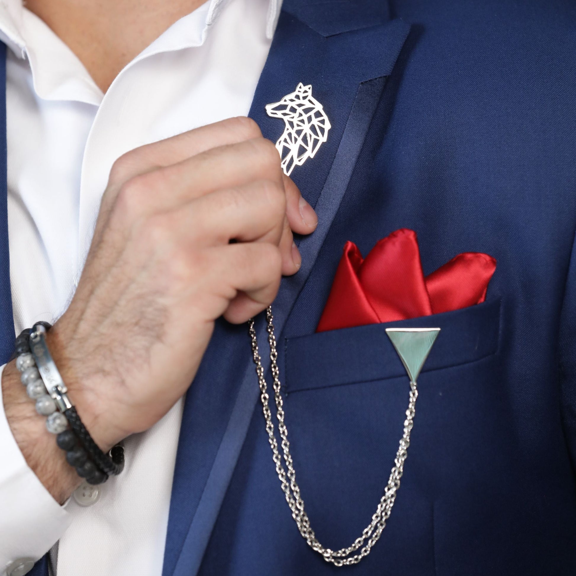 Man wearing a blue suit with a white shirt, red pocket square, and silver chain accessory.