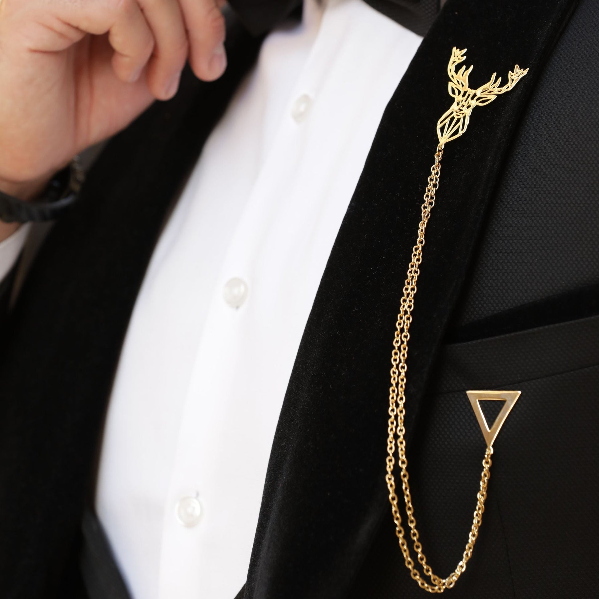 Man adjusting bow tie with a gold chain tie pin on a black suit.